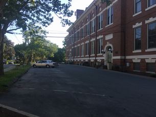 Photo looking slightly uphill at Municipal Bldg Parking lot running parallel to the bldb - Municipal building on left, greassy area on right