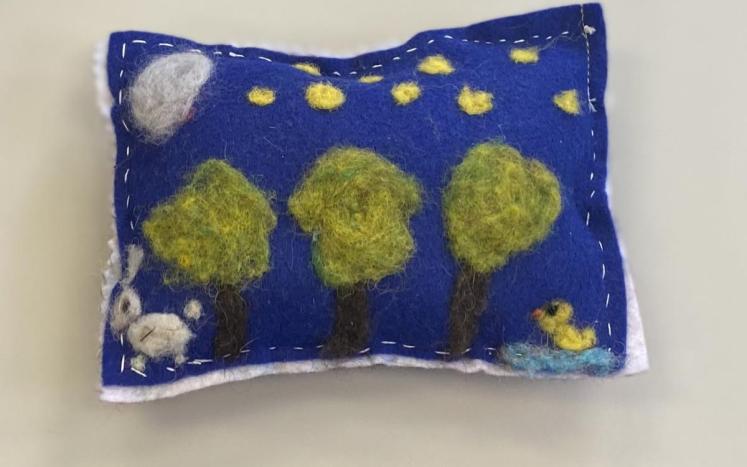 felted pillow with a scene of trees, clouds and small animals